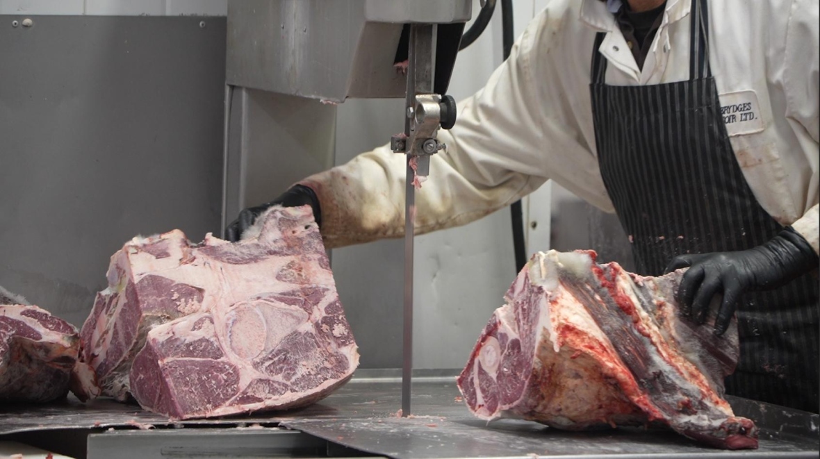 A butcher guides a huge piece of beef through a meat saw inside a butchery